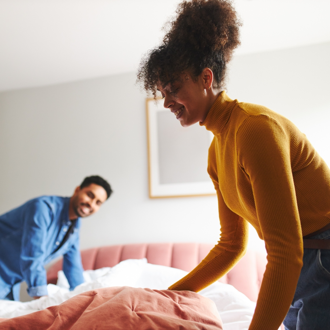 Couple smiling while making the bed