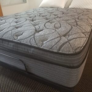 Angled view of grey Dutchcraft pillow-top mattress with tufted swirl quilting on a platform frame.