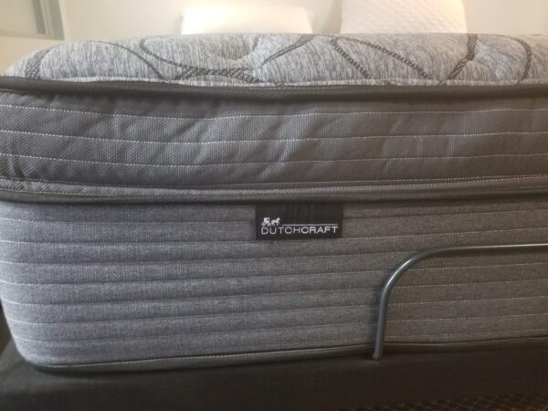 Side view of grey Dutchcraft pillow-top mattress on an adjustable base with brand label.