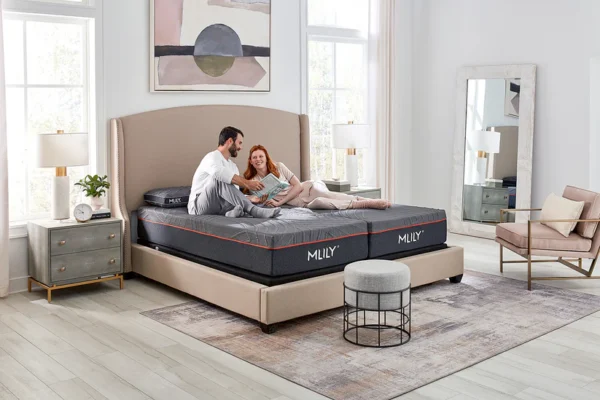 Couple lounging on a split-king MLILY bed with grey mattresses and red piping in a bright, modern bedroom.
