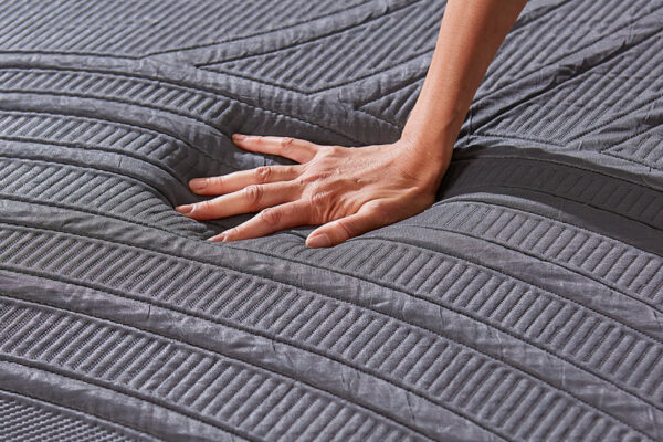 Close-up of a hand pressing into the textured grey MLILY PowerCool mattress cover, showing deep contouring.