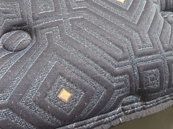 Close shot of blue mattress edge showing raised quilting, tuft button, and piped seam.