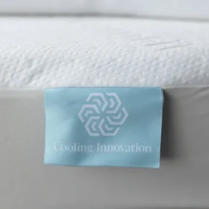 Detail of a blue “Cooling Innovation” satin tag sewn to the textured white mattress surface.
