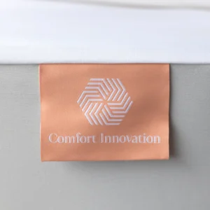 Peach “Comfort Innovation” tag stitched to the side of a white mattress protector.