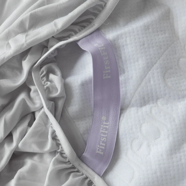 Light-grey fitted sheet turned inside out, displaying a lavender FirstFit® elastic identifier.