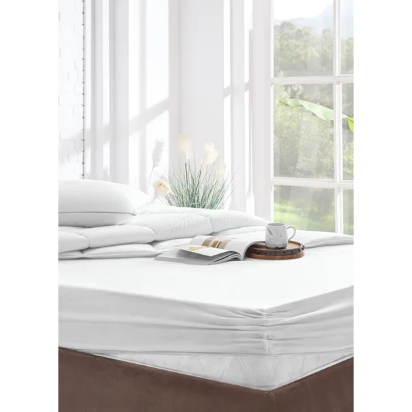 Bright room scene showing a neatly made bed with a white protector, stacked toppers, and a mug on a tray.