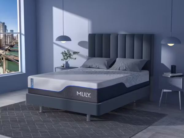 Loft-style room view of the MLILY mattress with blue piping, positioned near a city-scape window.